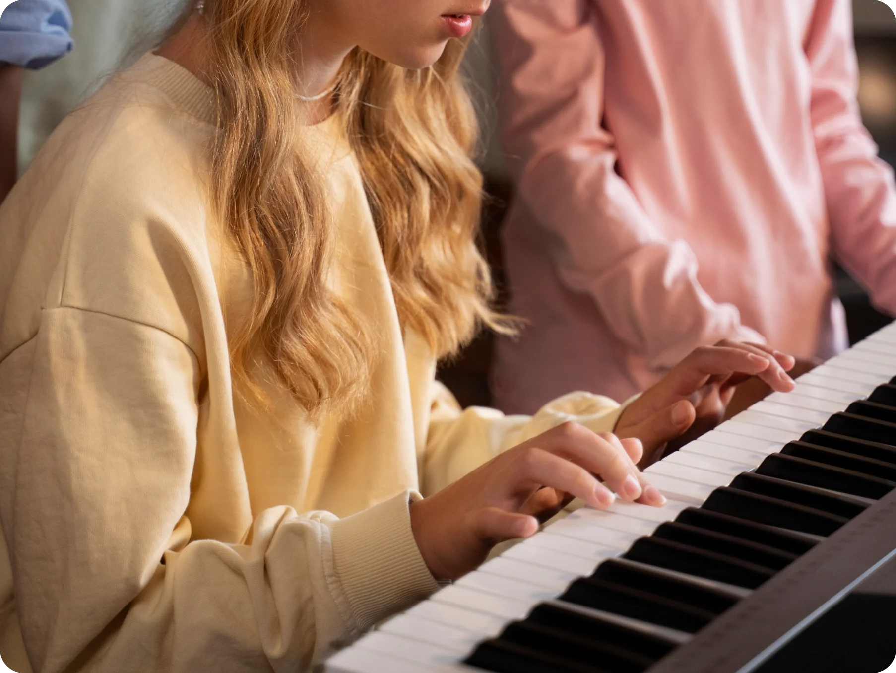 A young student plays a keyboard while her music teacher guides her hands